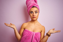Young Beautiful Woman Wearing Towel After Shower Over Isolated Pink Background Clueless And Confused Expression With Arms And Hands Raised. Doubt Concept.