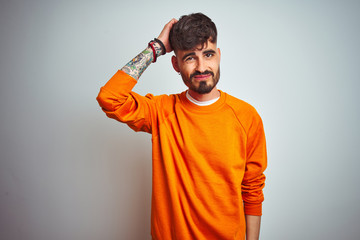 Sticker - Young man with tattoo wearing orange sweater standing over isolated white background confuse and wonder about question. Uncertain with doubt, thinking with hand on head. Pensive concept.