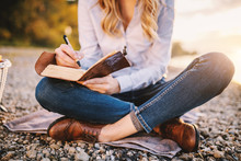 Cropped Picture Of Focused Fashionable Beautiful Caucasian Woman Sitting Near River And Holding Notebook.
