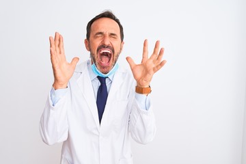 Middle age scientist man wearing coat and medical mask over isolated white background celebrating mad and crazy for success with arms raised and closed eyes screaming excited. Winner concept