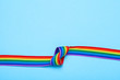 © adragan - Tape with a knot. LGBT Pride Rainbow Ribbon against blue background