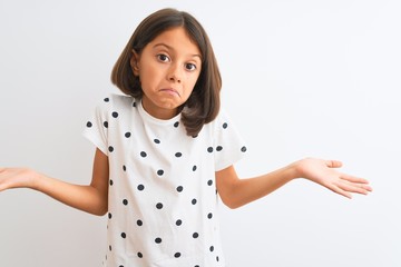 Poster - Young beautiful child girl wearing casual t-shirt standing over isolated white background clueless and confused expression with arms and hands raised. Doubt concept.