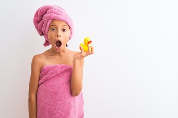 Poster - Beautiful child girl wearing shower towel holding duck over isolated white background scared in shock with a surprise face, afraid and excited with fear expression