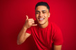 © Krakenimages.com - Young brazilian man wearing t-shirt standing over isolated red background smiling doing phone gesture with hand and fingers like talking on the telephone. Communicating concepts.