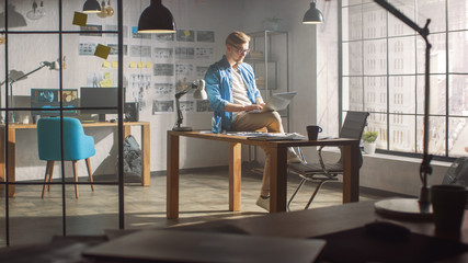 Wall Mural - Professional Creative Designer Sits on His Desk Holds Laptop on the Knees Early Morning while Working on the Project. Creative Designe and Gaming Content Development Studio