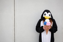 Beautiful, Young Woman In Penguin Costume Is Eating Deco Ice Cream In Front Of Concrete Wall