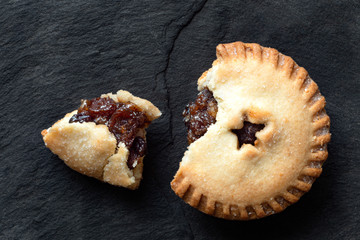 Poster - Broken open traditional british christmas mince pie with fruit filling isolated on black slate. Top view.