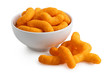 Extruded cheese puffs in a white ceramic bowl next to spilled cheese puffs isolated on white.
