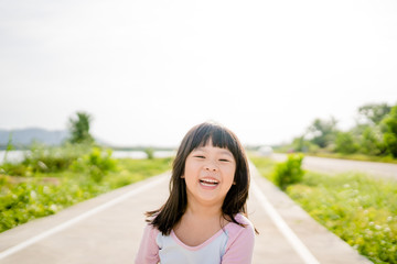 Wall Mural - Happy Little asian girl child showing front teeth with big smile, laughing and jogging in summer park in Japan : Healthy happy funny smiling face young adorable lovely female kid.Joyful portrait girl.