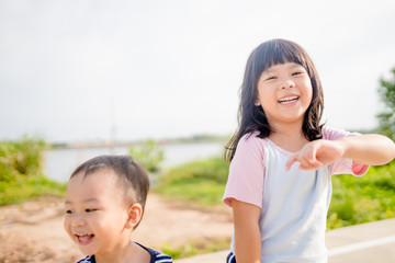 Wall Mural - Little sister walking exercise with her baby brother in the park.Toddler kid play with sibling holding hands and leading the way. Cute girl and baby Family with children.Love, trust and tenderness.