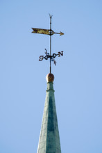 A WEATHER VANE Made As An Arrow With Directional Points Attached To A Post On Top Of A Tower Of A Building