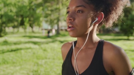 Canvas Print - An african american young fitness woman taking breathe and inserts earphones in her ears before running in the park