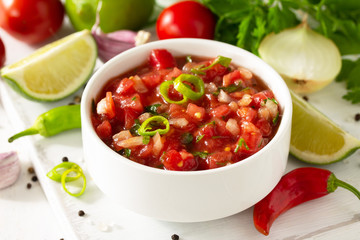 Traditional mexican homemade salsa sauce and ingredients on a white wooden table.