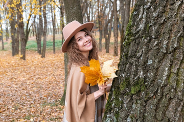 A girl walks through the autumn park at sunset. Boho style girl with hat and poncho. Girl with leaves in her hands.