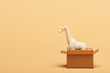White toy giraffe in cardboard box on yellow background, animal welfare concept