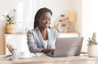 © Prostock-studio - Smiling afro businesswoman working on laptop in modern office
