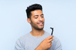 Young man shaving his beard over isolated blue background with happy expression