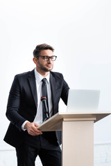 Wall Mural - businessman in suit standing at podium tribune and looking away during conference isolated on white