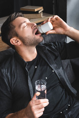 Wall Mural - high angle view of handsome man with panic attack taking pills and holding glass of water in apartment