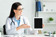 © LIGHTFIELD STUDIOS - beautiful positive doctor showing digital tablet with blank screen in clinic office