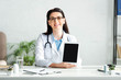 © LIGHTFIELD STUDIOS - attractive smiling doctor showing digital tablet with blank screen in clinic office