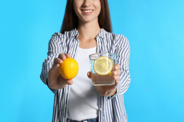 Wall Mural - Young woman with glass of lemon water on light blue background