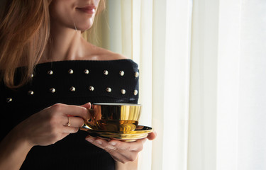 Woman with gold plated coffee cup by the window, soft sunlight, luxury lifestyle, copy space.