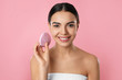 © New Africa - Young woman holding facial cleansing brush on pink background. Washing accessory