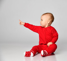 Wall Mural - Little toddler boy points finger up side in red infant bodysuit with free text space on gray full body