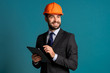© kohanova1991 - Young engineer businessman in suit jacket makes notes on tablet about building project, report. Businessman isolated on blue background as on construction. He is satisfied.