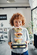 © Westend61 - Portrait of smiling businesswoman holding stack of takeaway food in office