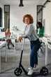 © Westend61 - Portrait of a smiling businesswoman with kick scooter in office