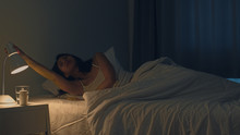 Beautiful Asian Young Woman Sleeping Cozily In Her Bedroom. Indian Female Hand Turning Off On Light Switch Near Bed In Room At Home In Late Night Ready To Sleep. Sweet Dreams And Relaxation Concept.