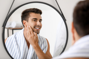 Handsome young man looking in mirror after shaving at home