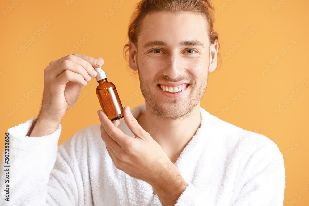 Handsome young man with cosmetic product on color background