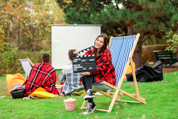 Poster - Happy young woman with movie clapper in outdoor cinema