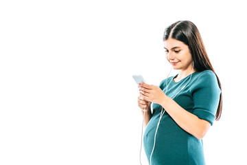 smiling pregnant girl using smartphone and listening music in earphones isolated on white