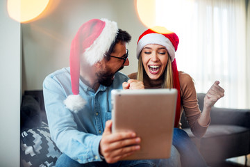 Wall Mural -  Love couple with Christmas hats on head using tablet and smiling