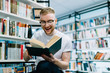 © BullRun - Happy man reading book in library
