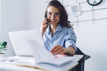 Smiling brown haired woman talking on smartphone in office