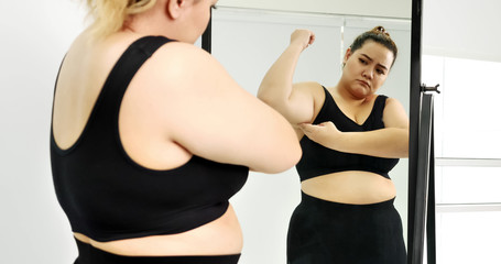 Chubby woman standing and looking at her arm in a mirror.