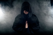 Man Dressed In A Dark Robe Looking Like A Cult Leader On A Smoky Or Foggy Background.  He Looks Like A Creepy Evil Villain