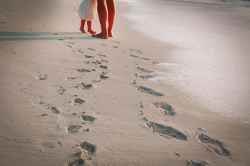 Wall Mural - mother and daughter walking on beach leaving footprint in sand