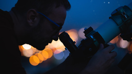 Wall Mural - astronomer with a telescope watching at the stars and moon with blurred city lights in the backgroun