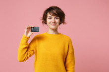 Smiling Young Brunette Woman Girl In Yellow Sweater Posing Isolated On Pastel Pink Wall Background Studio Portait. People Sincere Emotions Lifestyle Concept. Mock Up Copy Space. Hold Credit Bank Card.