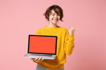 Wall Mural - Joyful young brunette woman in yellow sweater posing isolated on pink background. People lifestyle concept. Mock up copy space. Hold laptop pc computer with blank empty screen, doing winner gesture.