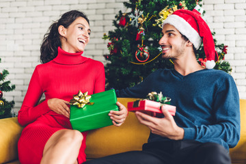 Romantic sweet couple in santa hats having fun decorating christmas tree and smiling while celebrating new year eve and enjoying spending time together.man giving gift box surprise to woman 