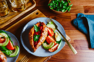 Baked sweet potato filled with red beans stewed in tomato paste served with avocado and cherry tomatoes on a plate. Healthy veggie recipe.