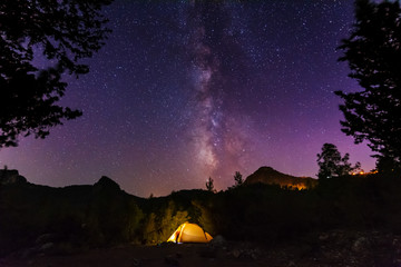 Wall Mural - Vertical landscape images with a night starry sky and a milky way against the backdrop of a yellow tourist tent, which is highlighted from the inside.