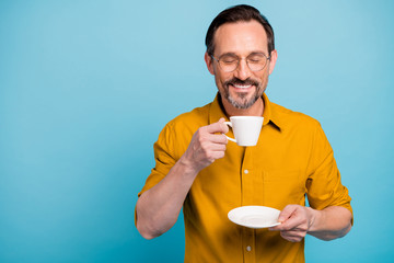 Poster - Portrait of positive cheerful man enjoy after work relax hold white coffee cup smell aromatic americano scent wear casual style clothing isolated over blue color background